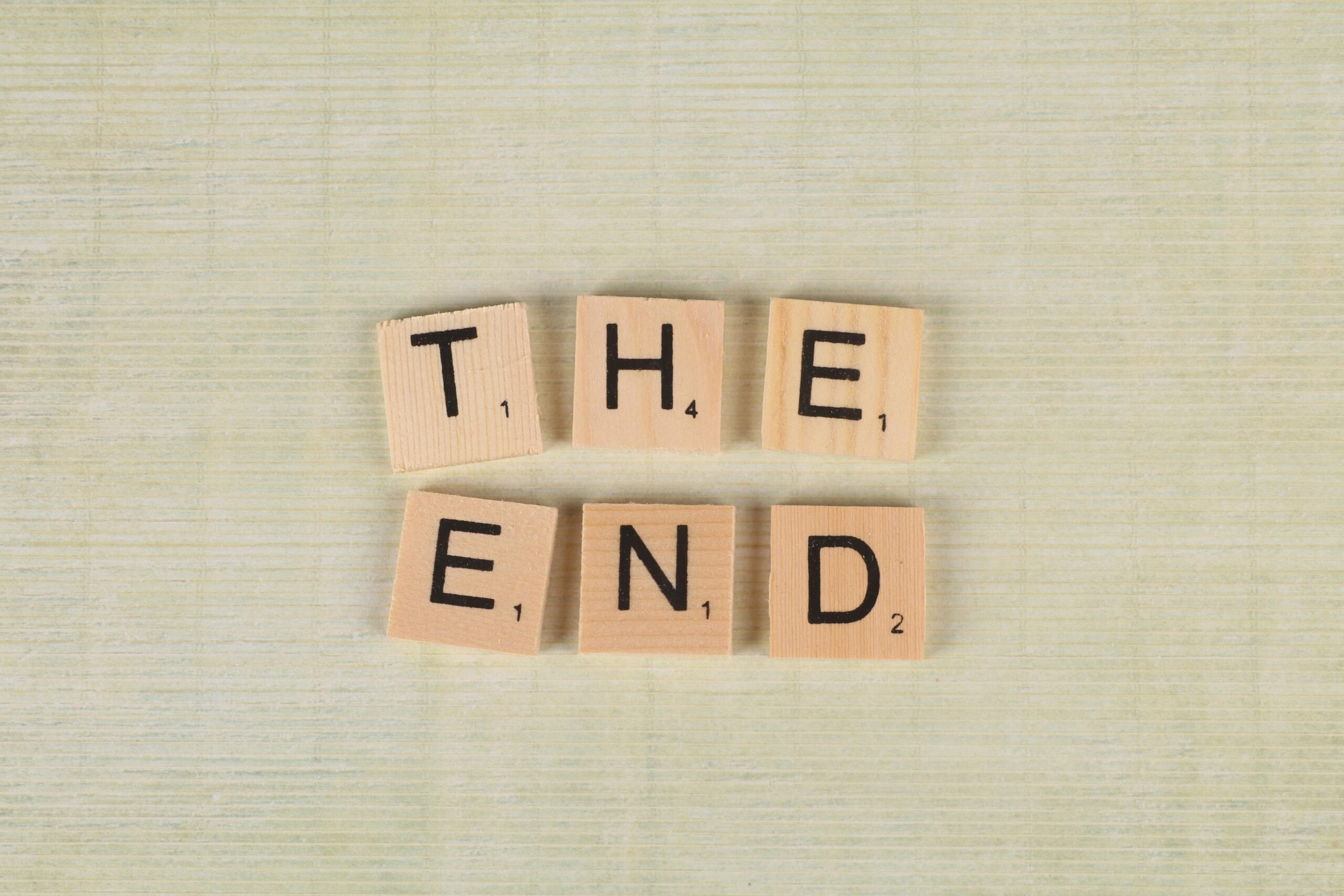 Close-up of Scrabble tiles spelling 'The End' on a simple wooden background for creative concepts.
